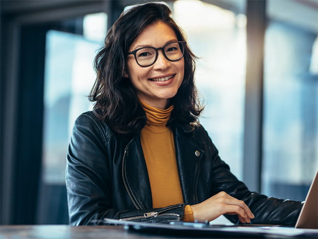 Smiling young professional woman sitting at table with laptop