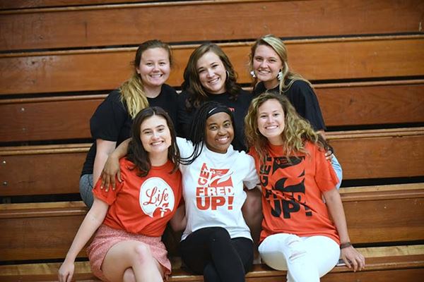 Diverse high school student girls hugging, posing close together on gym bleachers