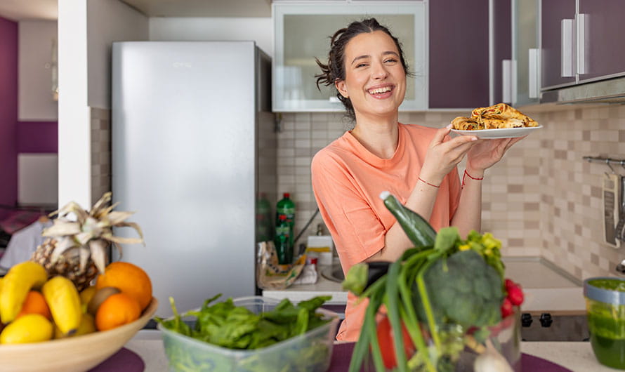 A joyful young woman showing healthy food she has prepared.