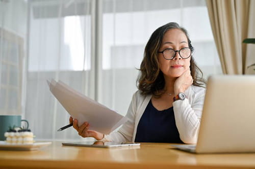 older Asian woman looking at a laptop sitting at her desk