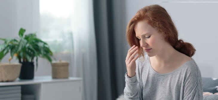 woman with red hair sitting on couch with hand to head