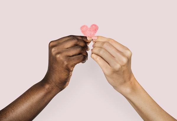 Two hands of different people holding a paper heart