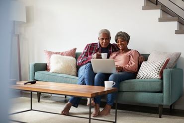 Older couple sitting on the couch together watching a webinar on a laptop